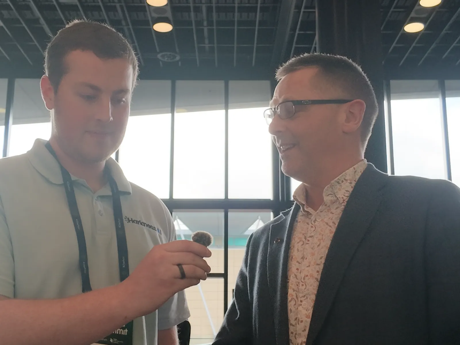 Grant Verhoeven in a floral shirt and blazer smiling while talking to Blake Harkness by the venue windows