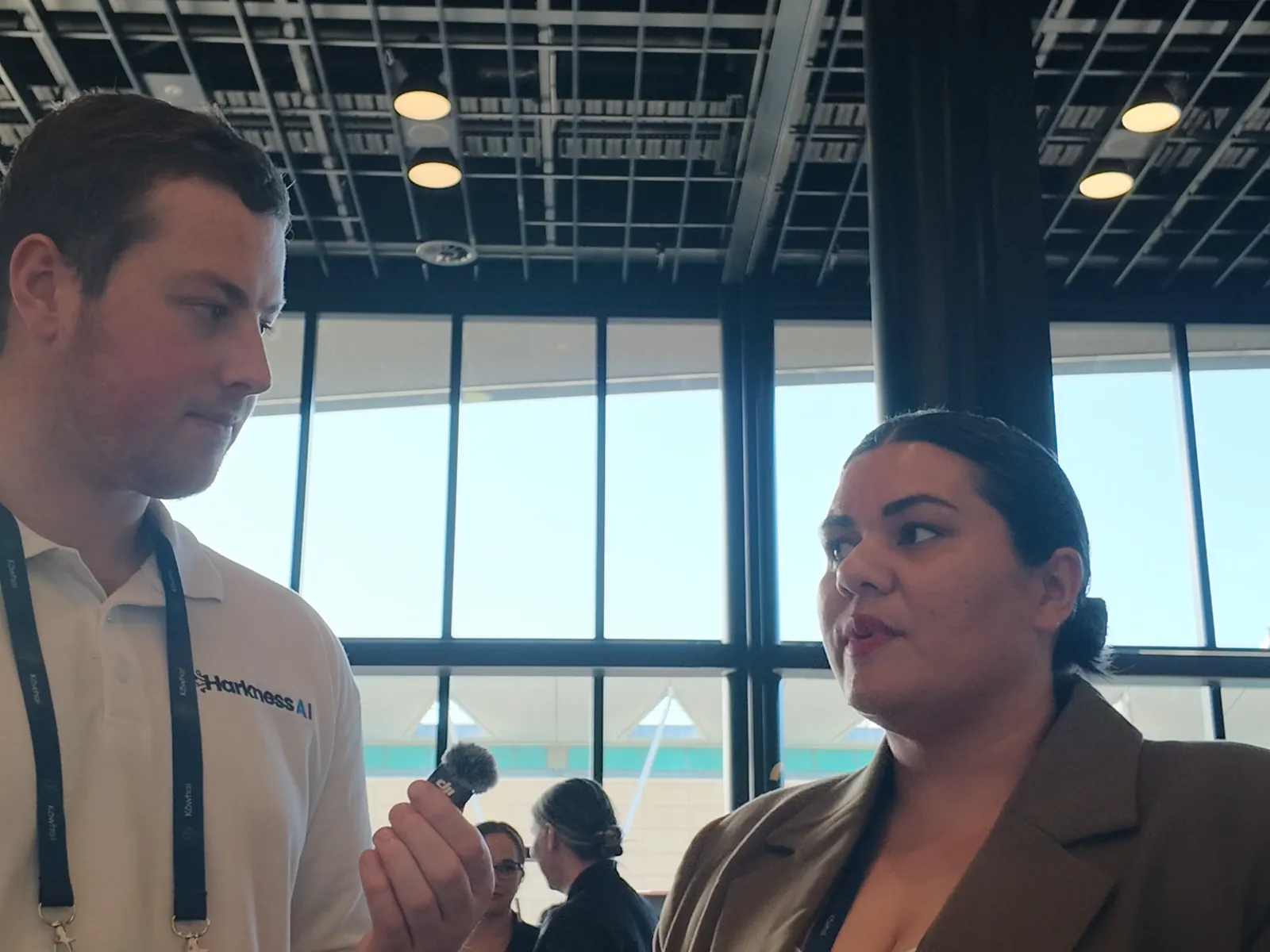 Lian Passmore talking to Blake Harkness in front of the tall windows of the summit venue