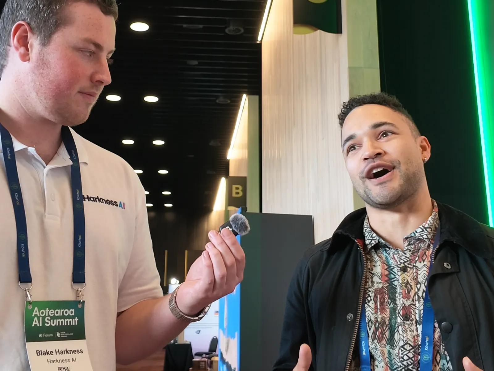 Michael Stanley talking enthusiastically to Blake Harkness beside a green-lit pillar marked C