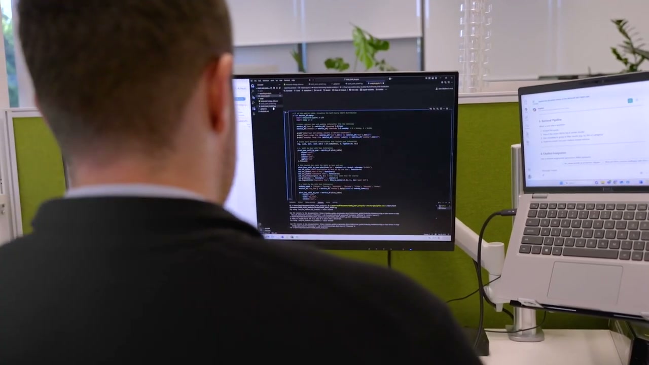 Blake working at desk with dual monitors showing code and development setup