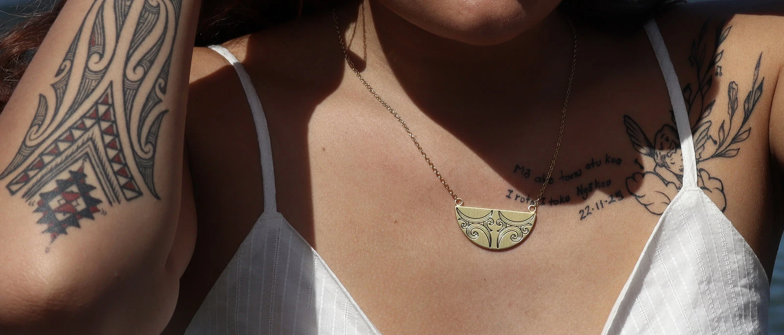 A gold Little Taonga breastplate pendant engraved with Maori design, worn on a fine chain
