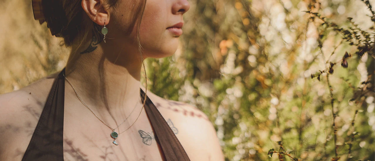 Pounamu earrings and a pounamu pendant from the Little Taonga collection, worn outdoors in warm light