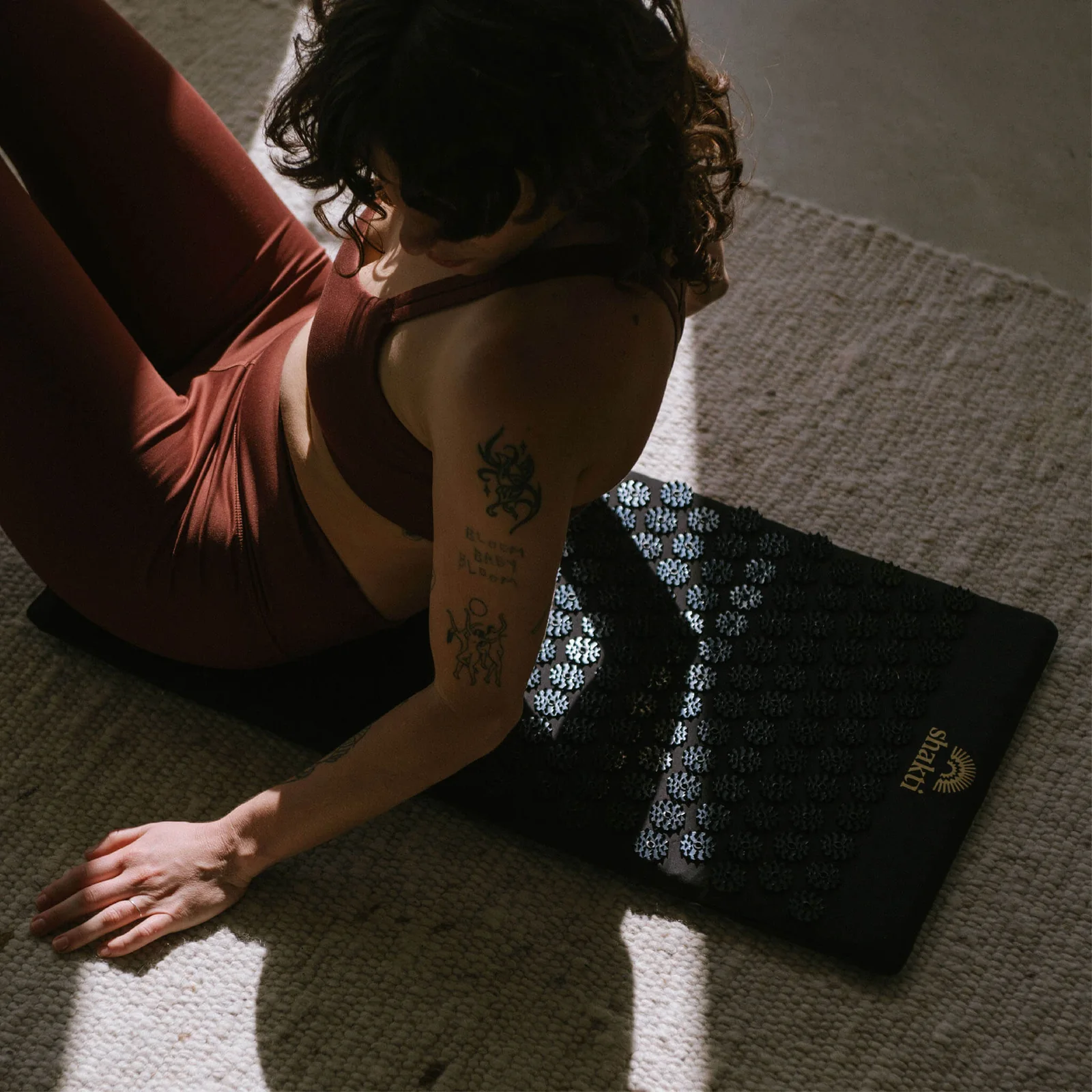 A woman sitting beside a black Shakti premium acupressure mat