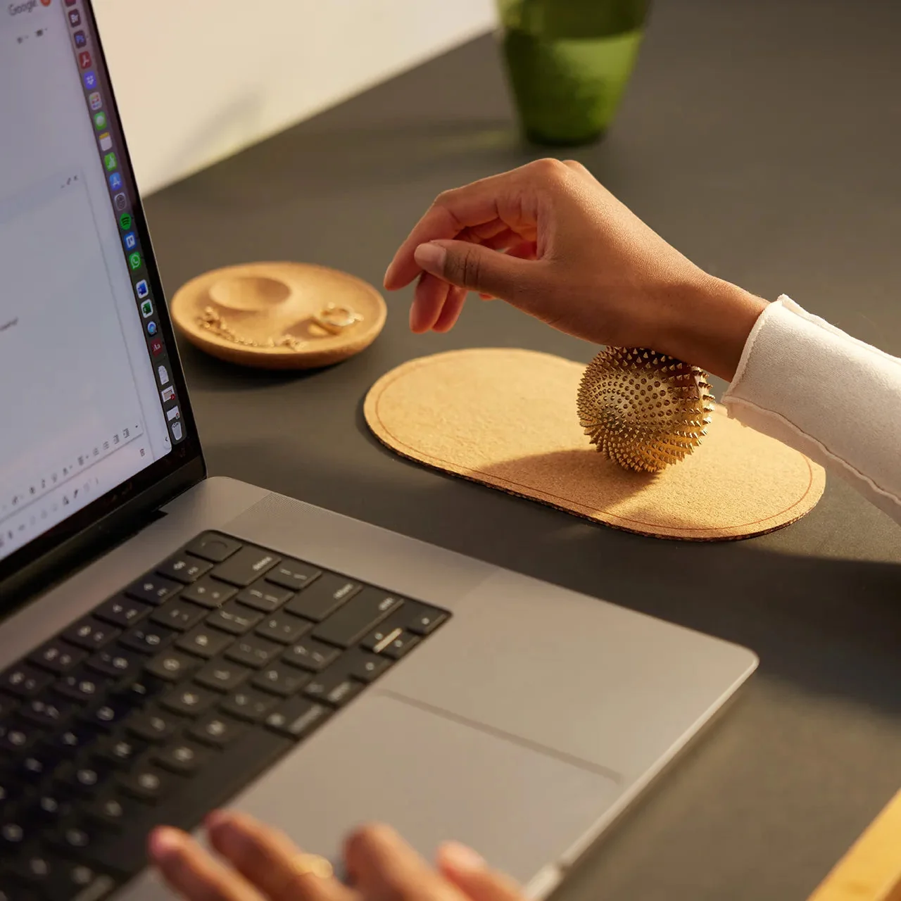 A Shakti acupressure ball on a cork tray beside a laptop on a desk