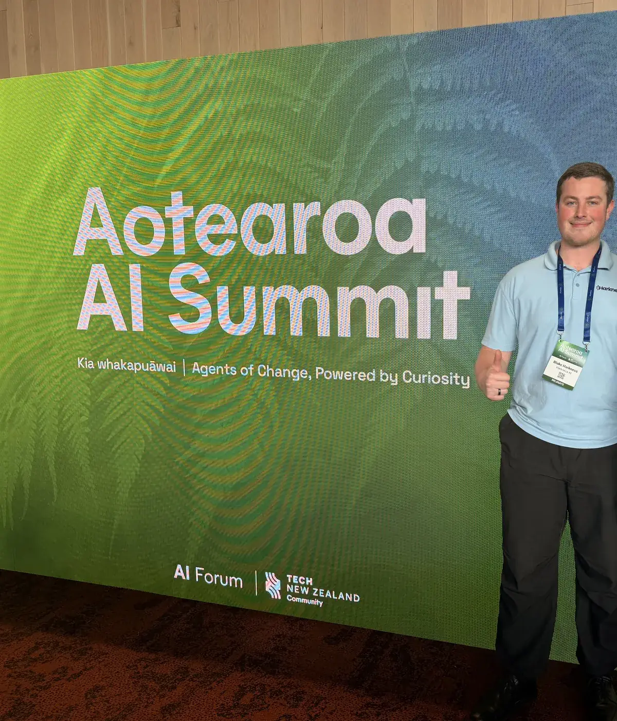 Blake Harkness in a Harkness AI polo in front of the Aotearoa AI Summit backdrop at Tākina, Wellington